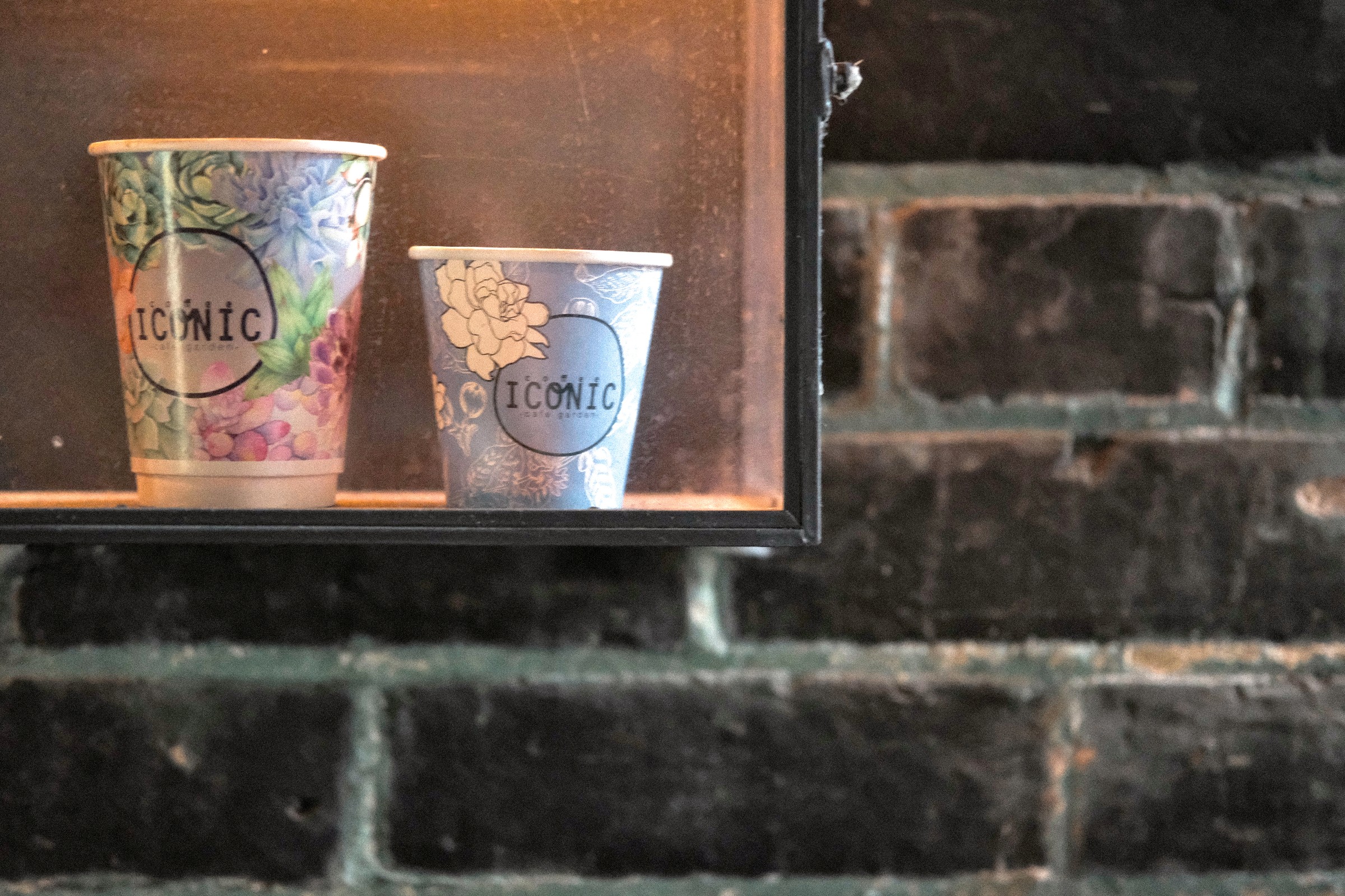 Two floral Coffee Iconic cups displayed against a brick wall