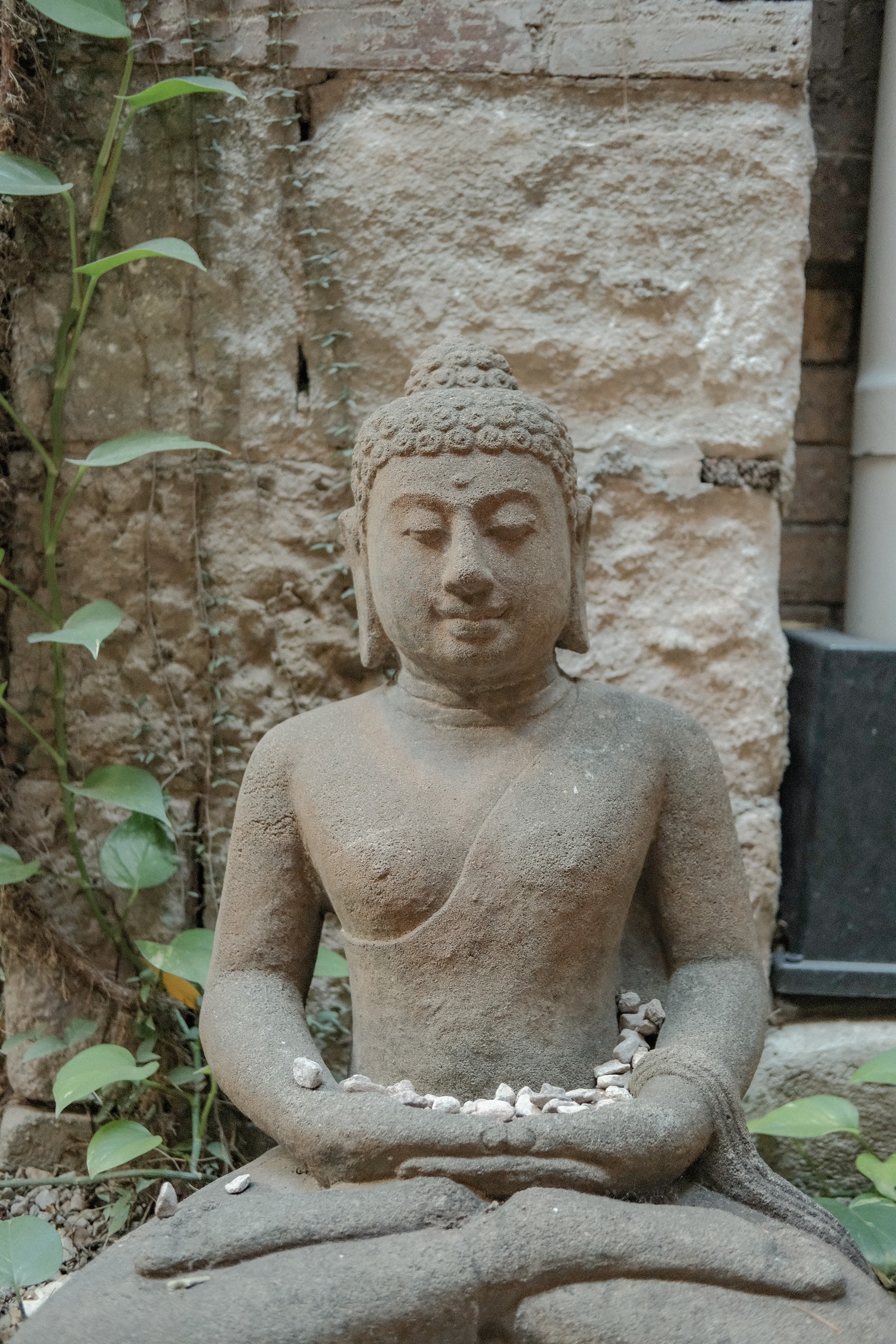 A seated Buddha sculpture against the garden stone wall